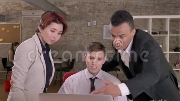 年轻的商业黑人男子说话指着笔记本电脑时白种人的男人和亚洲女人在现代视频的预览图