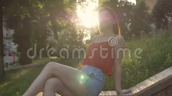 年轻迷人的女人姜发坐在街上的草地上挥舞着头发阳光灿烂视频的预览图