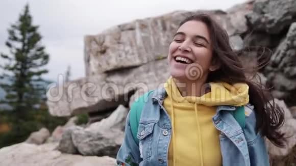 快乐的旅行者时髦女孩有着风的头发微笑着站在桑尼山顶时尚女性发型视频的预览图