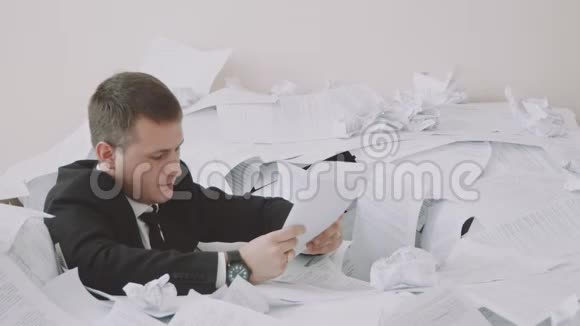 一个疲惫的雇员正坐在办公室里的一堆文件里在工作期间上班族正在经历视频的预览图