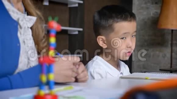 亚洲小男孩从地板上拿着落下来的笔和母亲一起学习坐在桌子书架和砖墙后面视频的预览图