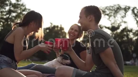 一群三个朋友在公园里喝着红色的塑料杯坐在绿色的草地上带着黑色和黑色视频的预览图