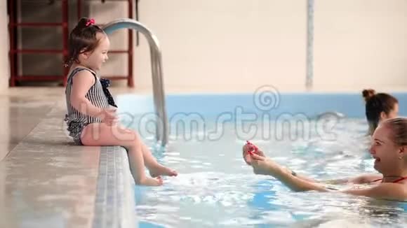 在游泳池里婴儿从旁边跳到水里慢慢地游向母亲视频的预览图