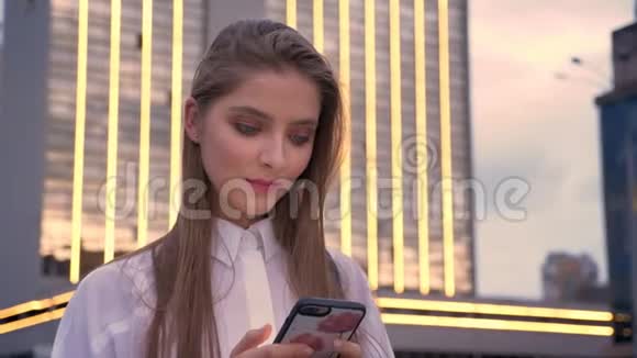 年轻迷人的精力充沛的女孩在夏天的日落时分看着她的智能手机交流理念视频的预览图