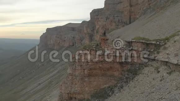 空中接近一位年轻的成年女子她背着背包到达史诗高原山脚下的岩石顶部视频的预览图