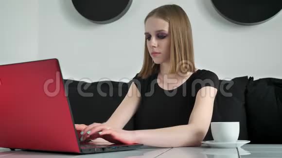 年轻的美女浓妆艳抹用手提电脑坐在沙发上浓墨重彩黑白咖啡背景视频的预览图