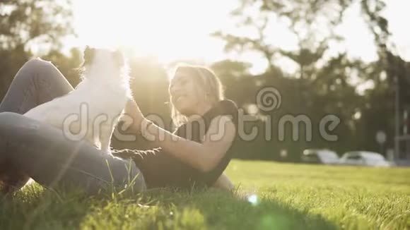 可爱的白种人女人躺在草地上她的小黑白狗坐在她的腿上主人爱抚和视频的预览图