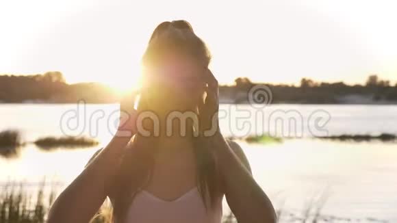 年轻迷人的女人在镜头里抚摸她的马尾辫微笑镜头耀斑河流和自然的肖像视频的预览图