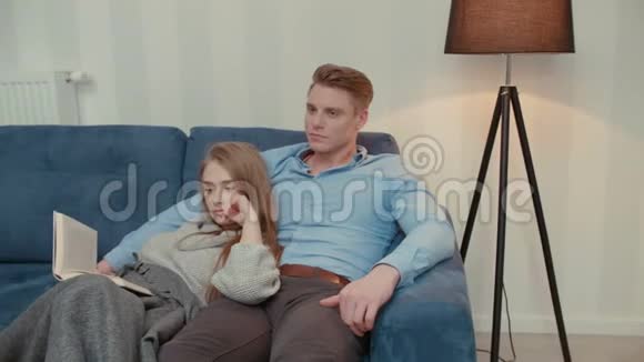 漂亮的夫妇坐在沙发上看电视和看书视频的预览图