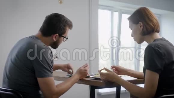 一对夫妇早上坐在他公寓的厨房里用刀叉吃煎蛋卷视频的预览图