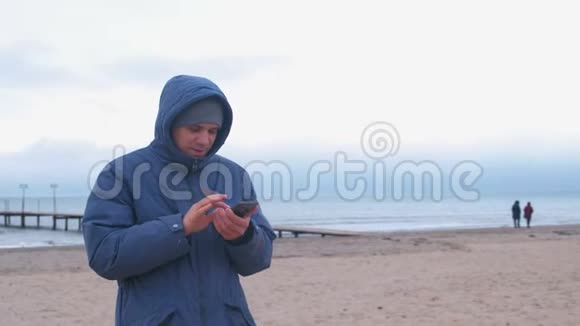 穿着蓝色羽绒服的人在海边的沙滩上打手机留言视频的预览图