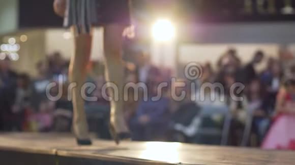 时装秀模特腿穿着高跟鞋在灯光和观众背景下穿着短裙登上领奖台视频的预览图