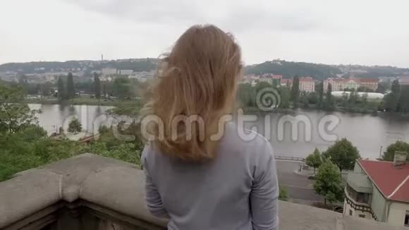 金发女人在阴天从阳台看城市风景镜头在移动视频的预览图