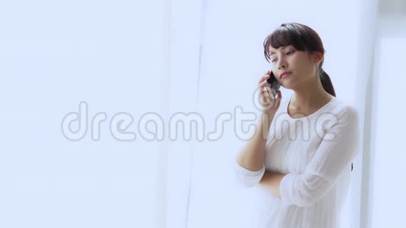 美丽的年轻亚洲女人站在卧室里压力很大女孩用手机说话严重视频的预览图