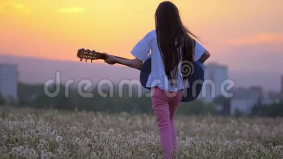 小女孩嬉皮士弹吉他就像蒲公英场上的流行歌星远离城市建筑的户外活动视频的预览图