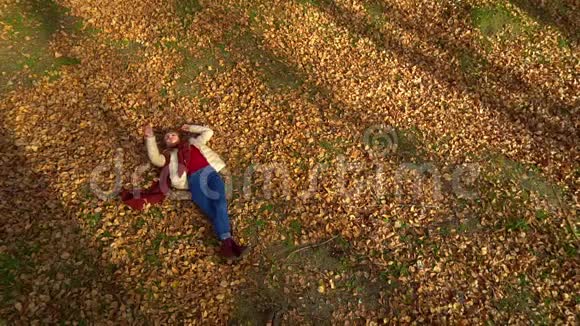 年轻迷人的女孩躺在秋天公园的叶子上视频的预览图
