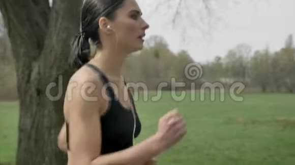 年轻有动力的女孩夏天在公园慢跑听音乐健康的生活方式运动观念侧视视频的预览图