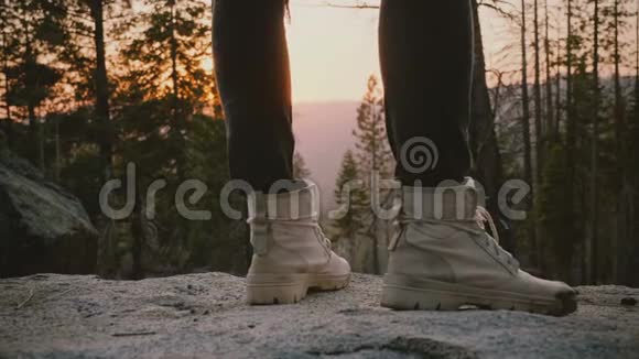 近距离拍摄的男性腿穿灰色沙漠鞋站在岩石上与史诗森林日落背景缓慢运动视频的预览图