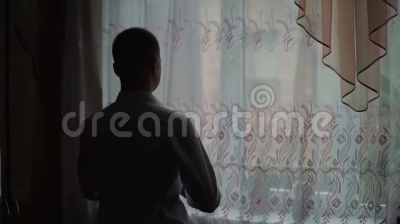 年轻人从家里的窗户欣赏风景穿上衬衫慢动作视频的预览图