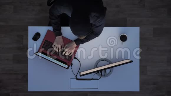 穿着黑色连帽衫的年轻人在笔记本电脑上打字晚上看着显示器坐在白色桌子后面喝着咖啡视频的预览图