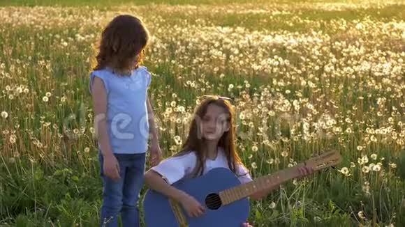 有趣的姐妹在蒲公英球场唱歌和弹声牛仔裤吉他在户外休闲的小女孩视频的预览图
