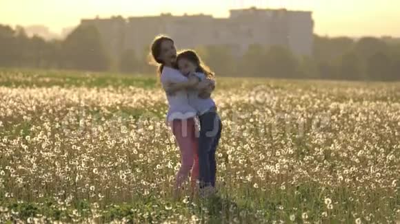 两个快乐的姐妹拥抱在户外城市建筑的背景下在蒲公英的草地上盘旋快乐的童年视频的预览图