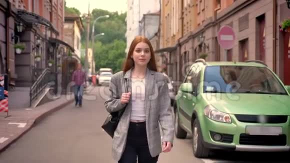 年轻漂亮的生姜女人走在城里摸着她的头发微笑着一个肩膀上拿着背包视频的预览图