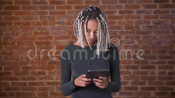 年轻的非洲女孩用平板电脑打字背景中的砖墙视频的预览图