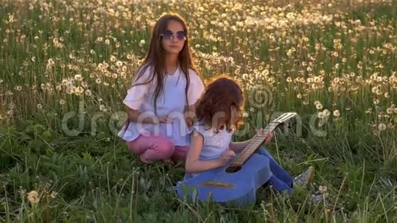 快乐的姐妹们在户外蒲公英球场弹吉他晚上快乐的童年概念自由和娱乐视频的预览图