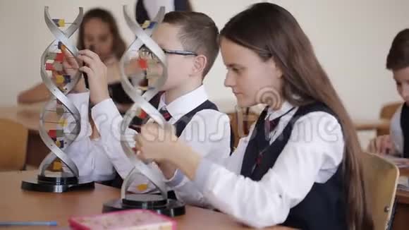 穿着校服的大学生正在研究DNA的布局并在坐着的时候通过显微镜观察视频的预览图