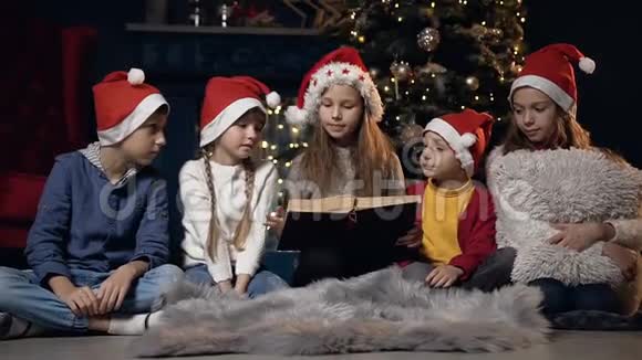 漂亮的孩子坐在圣诞树附近看书视频的预览图