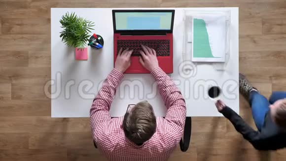 戴眼镜的年轻人在手提电脑上工作和打字女人给他咖啡顶头坐在桌子后面视频的预览图