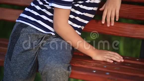 一个穿裤子和运动鞋的男孩坐在长凳上挥舞着腿夏日日落视频的预览图