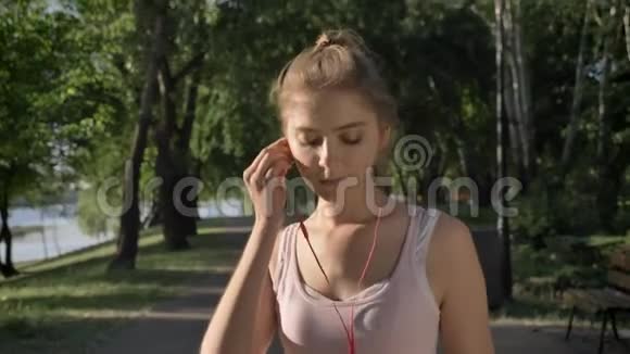 年轻漂亮的女人戴着耳机早上开始在公园里跑步微笑着视频的预览图