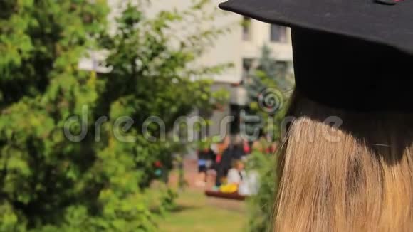 戴毕业帽的女生看着快乐的学生向空中抛帽子视频的预览图