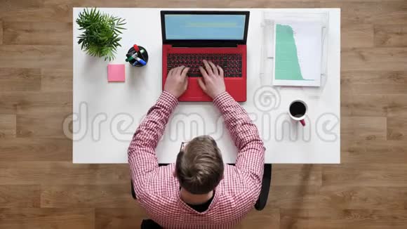 戴眼镜的年轻人在笔记本电脑上工作打字坐在桌子后面拿着咖啡和文件视频的预览图