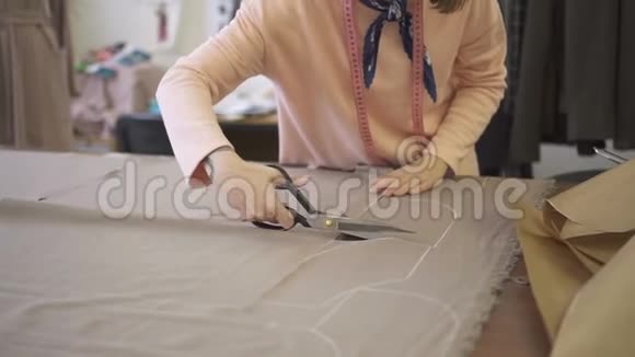 年轻女裁缝正在用剪刀剪布在工作过程中站在桌子旁背景上有布视频的预览图