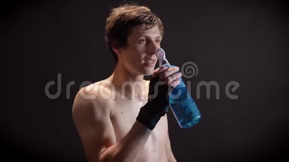 年轻的白种人无胸拳击手从瓶子里喝水休息看镜头黑色背景50fps视频的预览图
