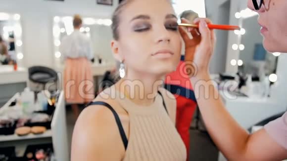慢动作视频年轻漂亮的时尚模特坐在大镜子旁边一边用灯泡化妆视频的预览图