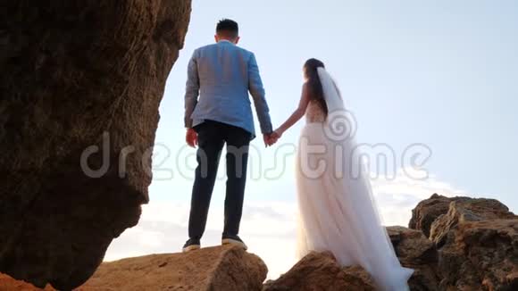 无法辨认的新婚夫妇在日落或日出背景下牵手新娘和新郎站在海边的户外视频的预览图