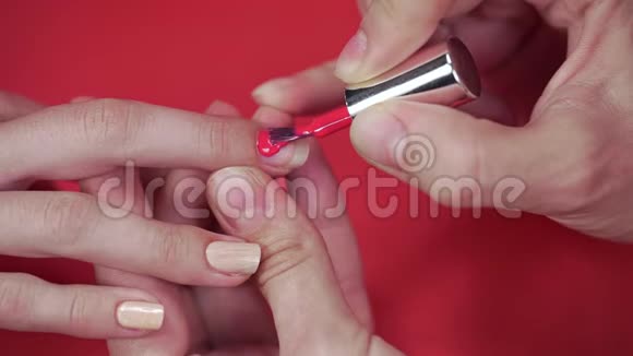 摩尼教客户的指甲用米色涂指甲油涂在红色背景化妆品和指甲上并将指甲贴紧视频的预览图
