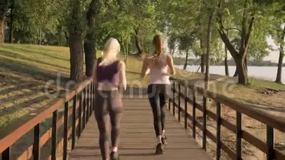两位年轻漂亮的女跑步者在公园跨桥慢跑减肥健身模特跑步从后面观看视频的预览图