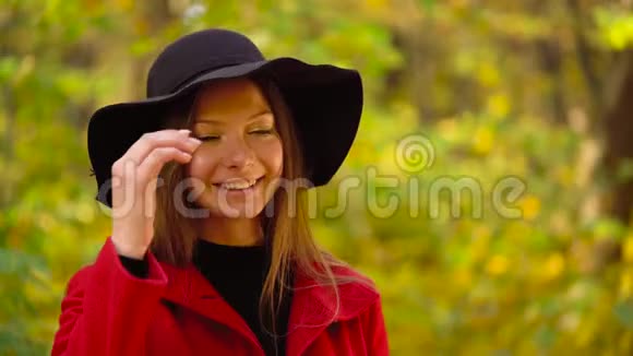 秋天森林中一个美丽的微笑女孩戴着一顶黑色帽子前景是一片黄色的枫叶视频的预览图