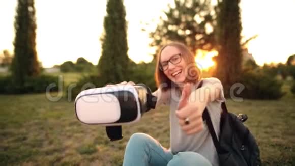 有选择性地关注虚拟现实眼镜在一个年轻的微笑女孩的手中显示拇指视频的预览图