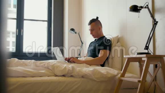 帅哥早上在一张带笔记本电脑的床上工作在漂亮的平板电脑里工作视频的预览图