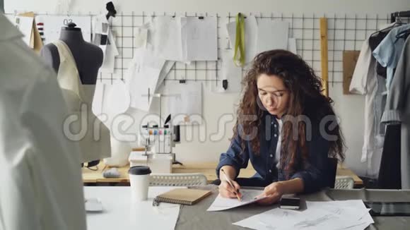 年轻女性时装设计师正在现代车间的办公桌上画女士服装素描人体模型缝纫用品视频的预览图