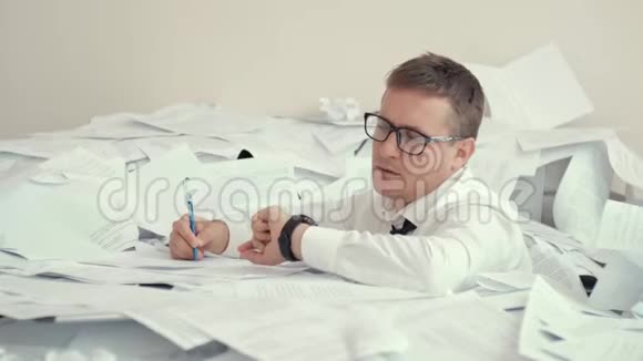 一个戴眼镜的疲惫的年轻人坐在一堆文件和签名文件里因为疲劳一个男人看起来很有希望视频的预览图