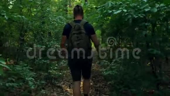 一个背着背包的留着胡子的人穿过一片茂密的森林出现在一片森林的空地上摄像机跟着他移动自然乔视频的预览图