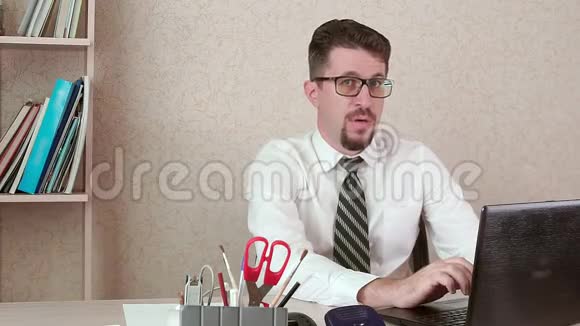 一个男人是一个办公室工作人员胡子和眼镜狡猾地看着一台笔记本电脑视频的预览图