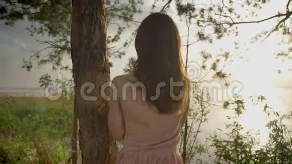 年轻美丽的姜笑着在森林里的沙滩上笑着的女孩站在树旁大自然剪影看着视频的预览图